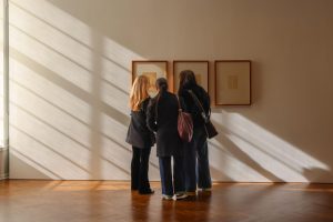 Tre studenti osservano quadri su una parete soleggiata di una galleria.