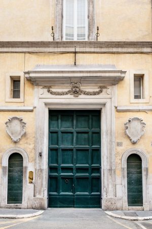 Facade of a historic building with a large central green door, a carved stone mask, and two smaller side entrances.