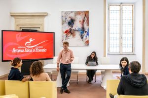 Studenti che interagiscono in un'aula universitaria con uno schermo sullo sfondo che mostra il logo European School of Economics.