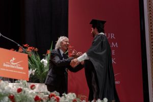 Elio D'Anna, ESE President and Founder, Congratulates a graduate on stage beneath the ceremony's theme, 