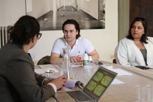 Primer plano de un estudiante sosteniendo un lienzo pequeño con una carita de pan de oro y un pincel.