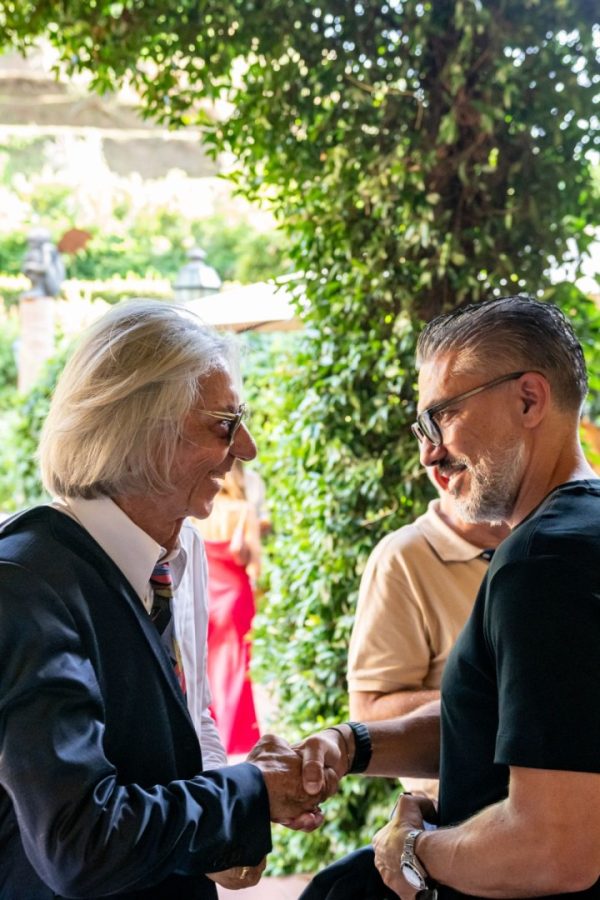 Due uomini si stringono la mano sorridendo all'aperto durante l'evento ESE Milano con The Longevity Suite.