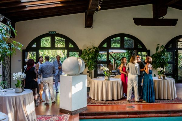 Ospiti conversano attorno a tavoli rotondi in un'elegante sala con finestre ad arco a ESE Milano.